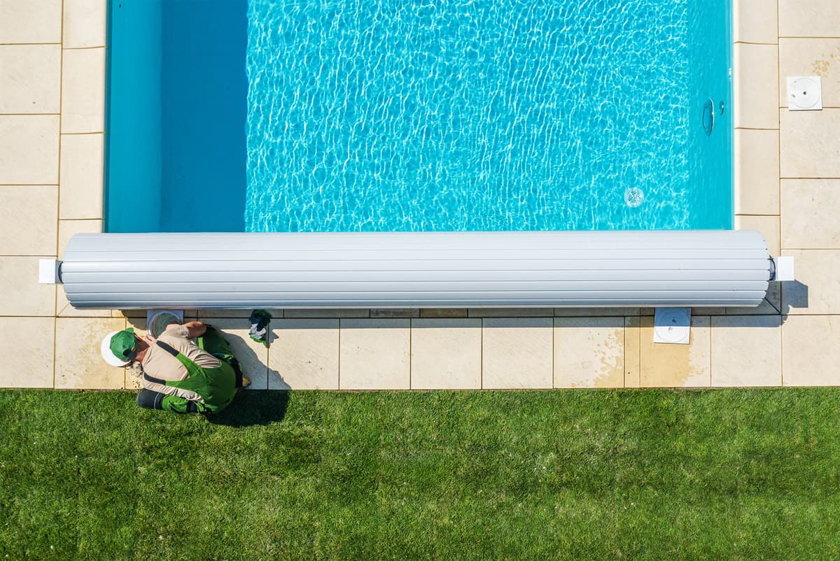 Aerial view of a technician servicing a pool cover roller at the pool edge