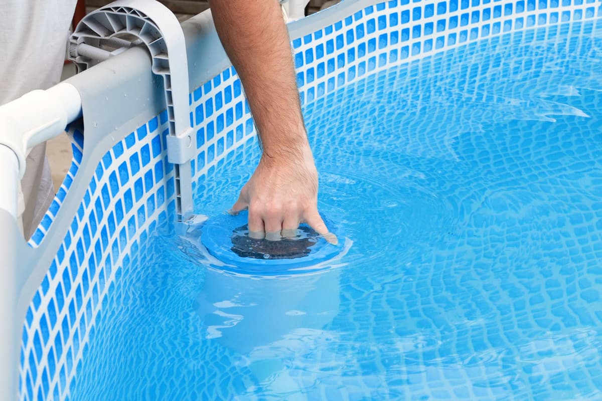 Hand reaching into a skimmer basket on an above-ground pool