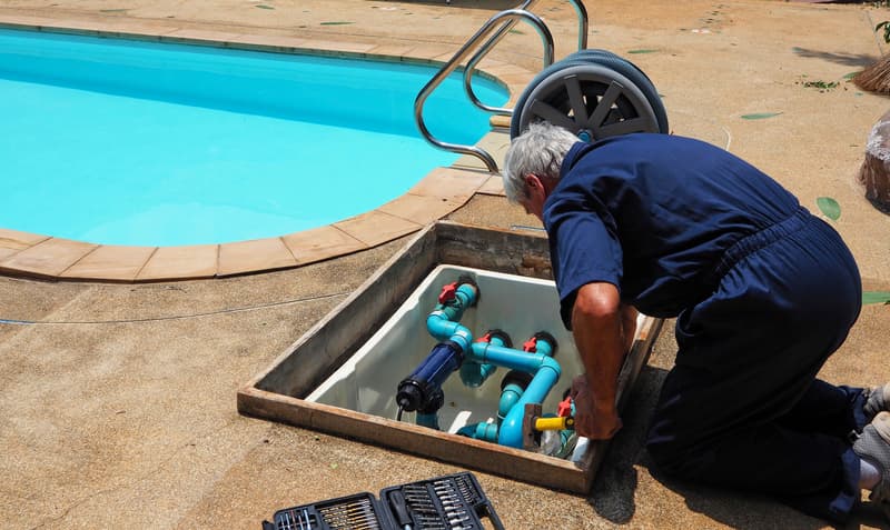 Technician repairing pool pump and valve plumbing in an equipment vault