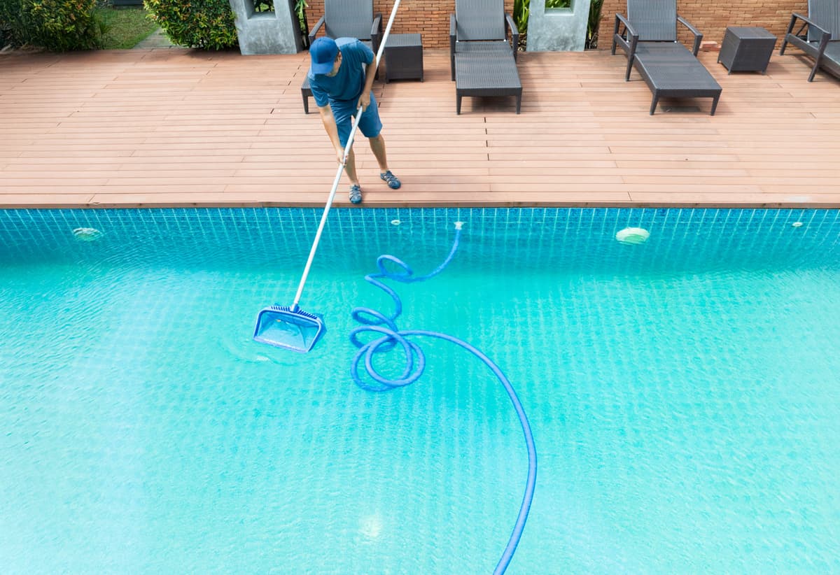Pool technician in blue uniform skimming debris from a swimming pool